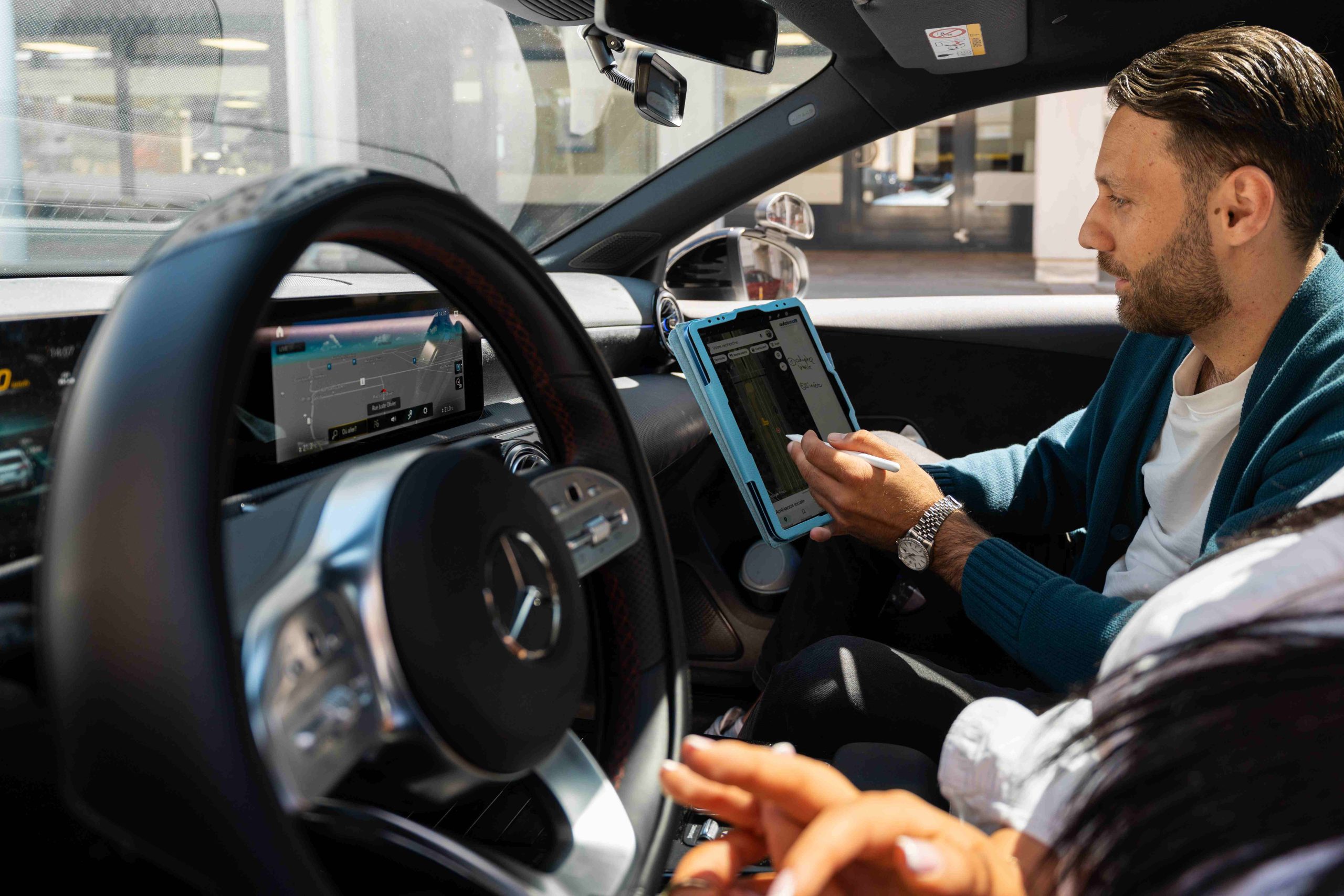 Moniteur utilisant une tablette et une miniature de voiture pour expliquer les priorités et le positionnement en intersection à une élève au volant d'une Mercedes